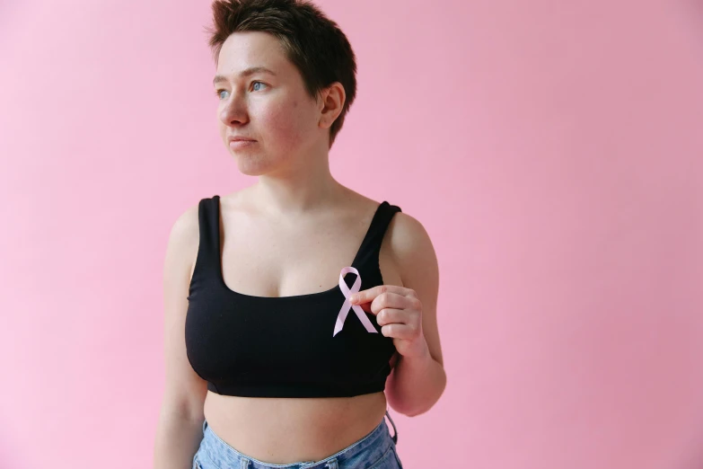 a woman holding a pink ribbon in front of a pink background, by Carey Morris, pexels contest winner, wearing a cropped black tank top, health supporter, very very very pale skin, with a black background