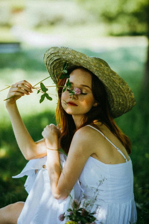a woman sitting in the grass with a flower in her hand, inspired by Konstantin Somov, pexels contest winner, renaissance, white hat, branches sprouting from her head, natural skin, holding a rose