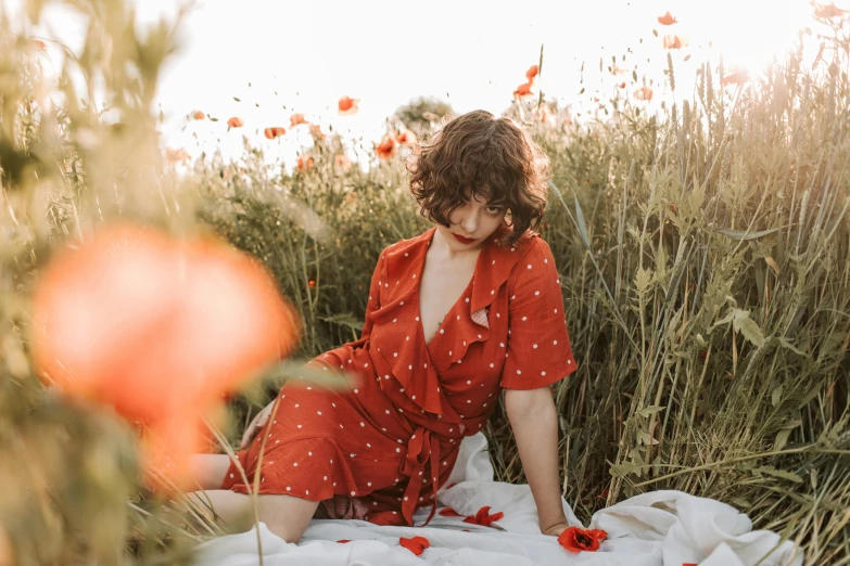 a woman sitting on a blanket in a field of flowers, an album cover, pexels contest winner, figuration libre, red jumpsuit, polka dot, photoshoot for skincare brand, light red and deep orange mood