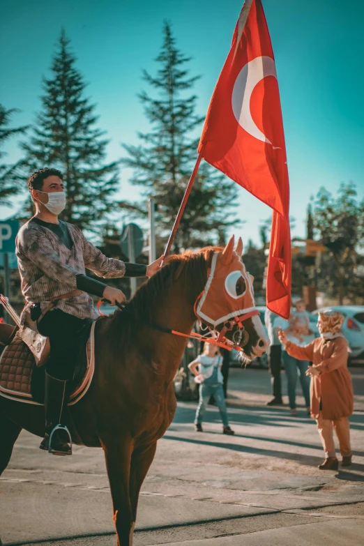 a man riding on the back of a brown horse, a colorized photo, pexels contest winner, red pennants, people are wearing masks, turkey, 🚿🗝📝