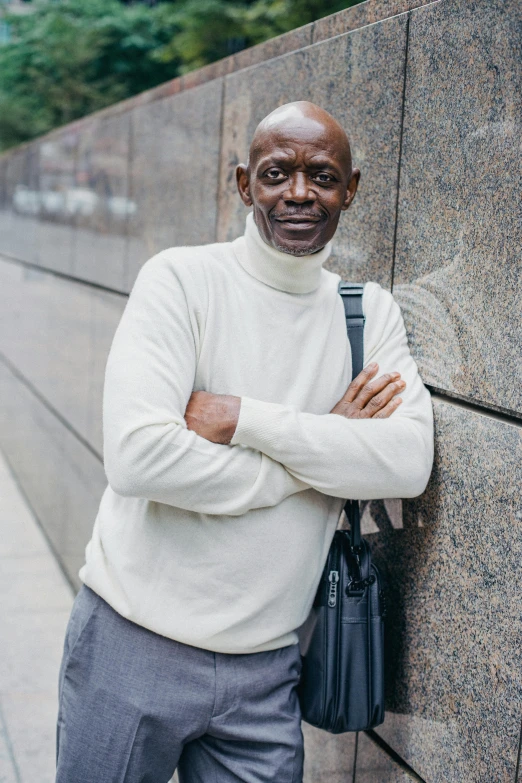 a man leaning against a wall with his arms crossed, a photo, by William Berra, grey skinned, 15081959 21121991 01012000 4k, on sidewalk, wearing turtleneck