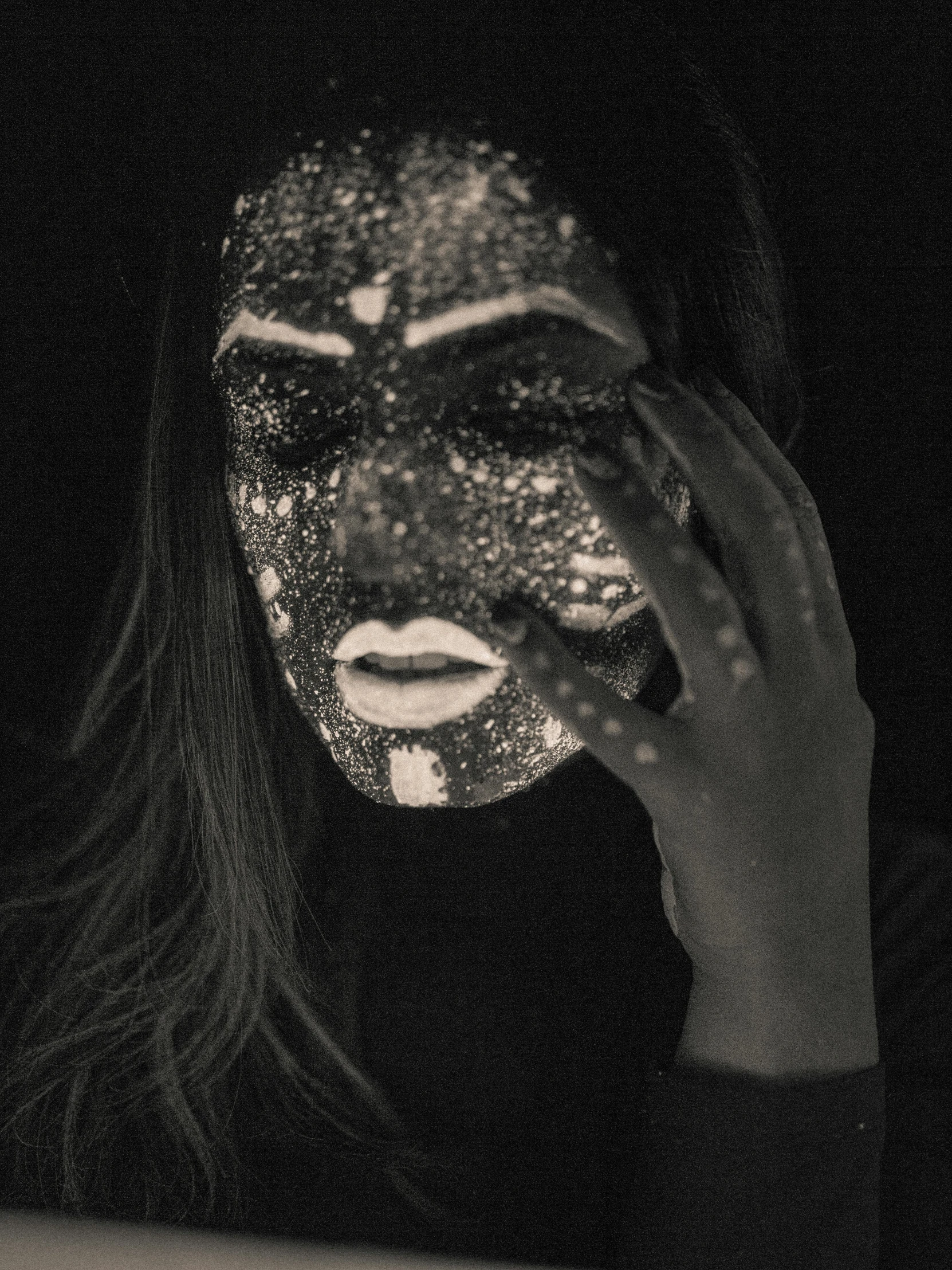 a black and white photo of a woman with glitter on her face, a black and white photo, pexels contest winner, transgressive art, black mask, hands shielding face, day - glow facepaint, grainy damaged photo