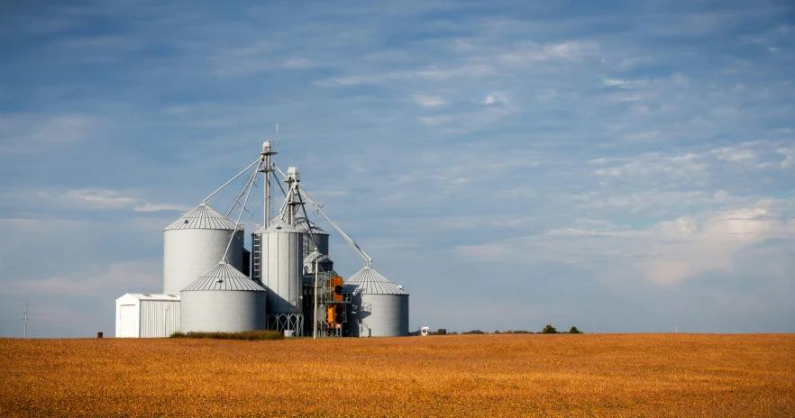 a couple of silos sitting on top of a dry grass field, pexels contest winner, midwest town, no cropping, industries, combine