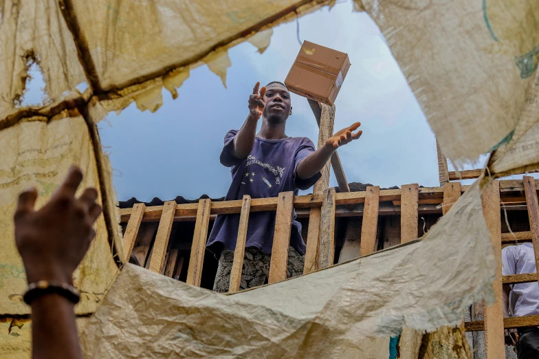 a man standing on top of a roof holding a box, happening, slums, window open, thomas kinade, collapsed ceiling