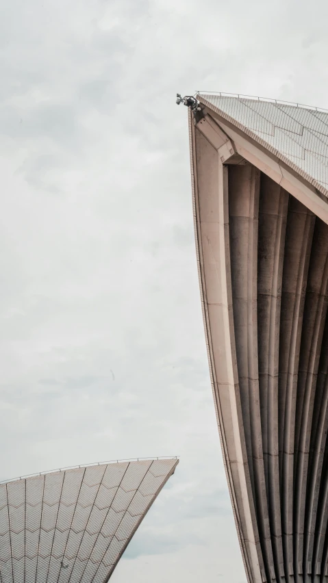 a couple of people that are standing in front of a building, an album cover, by Andrew Allan, unsplash contest winner, brutalism, sydney opera house, 3/4 view from below, detail structure, winged