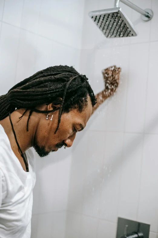 a man with dreadlocks standing in a bathroom, trending on pexels, water dripping off him, comforting, plain background, facing away