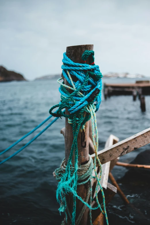 a boat sitting on top of a body of water, a colorized photo, pexels contest winner, environmental art, rope, cyan and green, a wooden, yarn