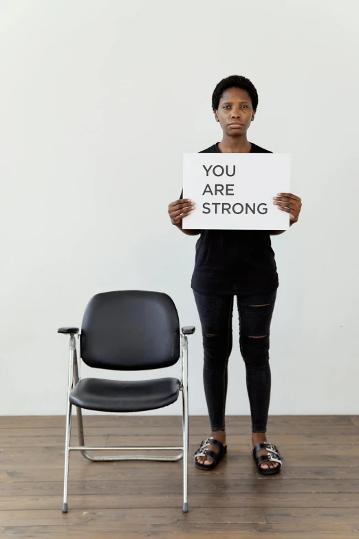 a woman holding a sign that says you are strong, chair, profile image, emmanuel shiru, studio photo