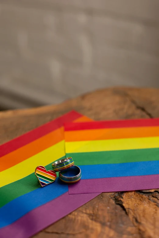 a pair of wedding rings sitting on top of a rainbow colored ribbon, inspired by Okuda Gensō, a wooden, to