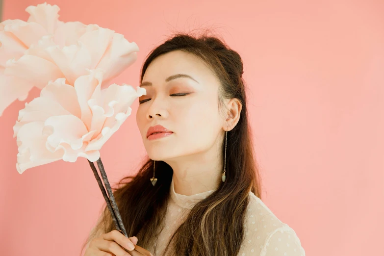a woman holding a flower in front of her face, inspired by helen huang, trending on pexels, aestheticism, pink background, she is holding a long staff, puffy lips, profile image