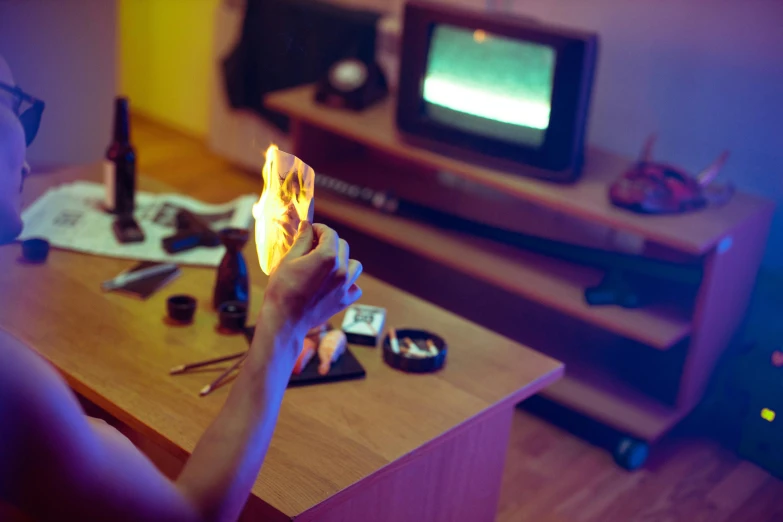 a person sitting at a table with a cell phone in their hand, an album cover, inspired by Elsa Bleda, pexels contest winner, geforce rtx 3090 on fire, watching tv, holding a torch, cardistry