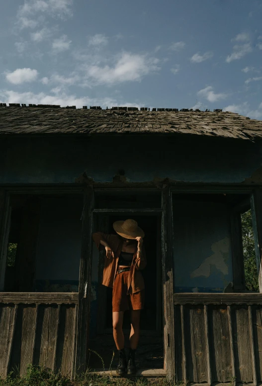 a man that is standing in the doorway of a house, by Attila Meszlenyi, pexels contest winner, woman with hat, ukrainian, gif, blue sky