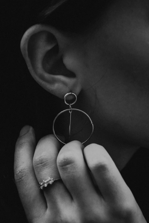 a black and white photo of a woman wearing a pair of earrings, minimalism, circle, silver jewellery, dark moody, [ metal ]