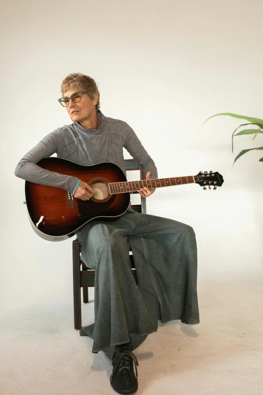 a woman sitting in a chair playing a guitar, by Winona Nelson, jamie lee curtis, androgynous male, high quality image, trending photo