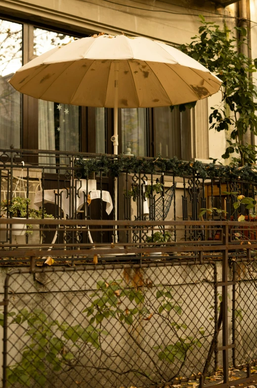 an umbrella sitting on top of a fence next to a building, inspired by André Kertész, art nouveau, patio, kreuzberg, warm shading, eating outside