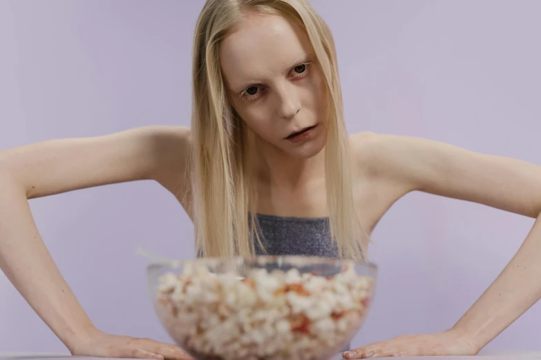 a woman sitting at a table with a bowl of popcorn, an album cover, inspired by Gottfried Helnwein, trending on pexels, die antwoord ( yolandi visser ), patricia piccinini, movie still 8 k, ellie bamber fairy