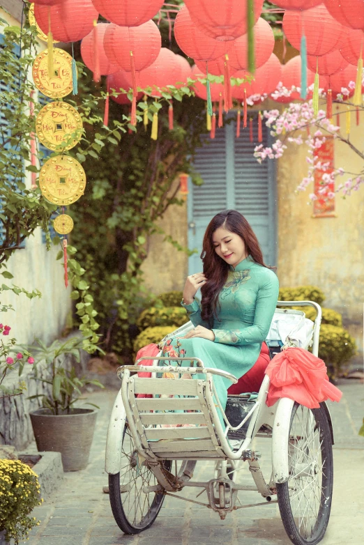 a woman in a green dress sitting on a bike, a picture, inspired by Tan Ting-pho, pexels contest winner, happening, blue colored traditional wear, square, spring day, [ colourful