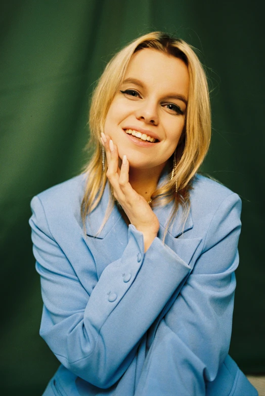 a woman in a blue suit posing for a picture, an album cover, by Sara Saftleven, dafne keen, close up of a blonde woman, happily smiling at the camera, hand on cheek