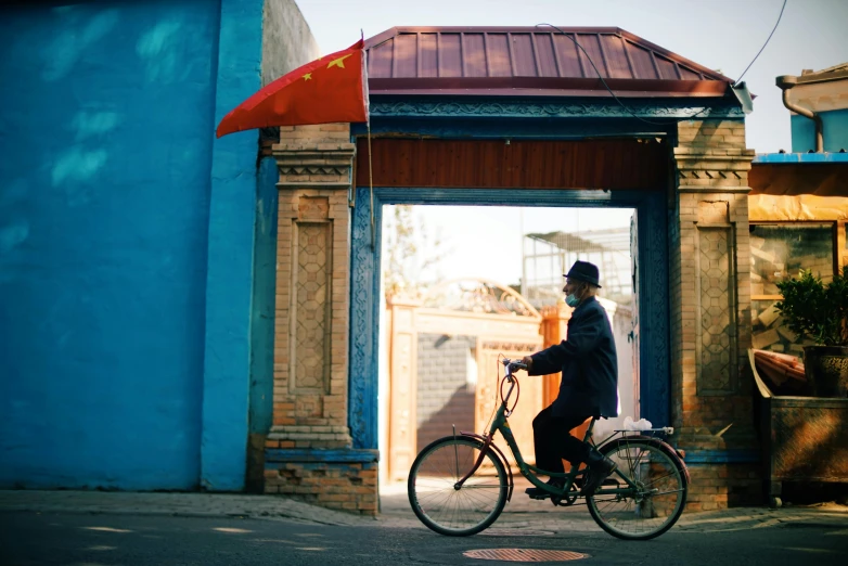 a man riding a bike in front of a blue building, mongol, dreamy chinese town, profile image, conde nast traveler photo