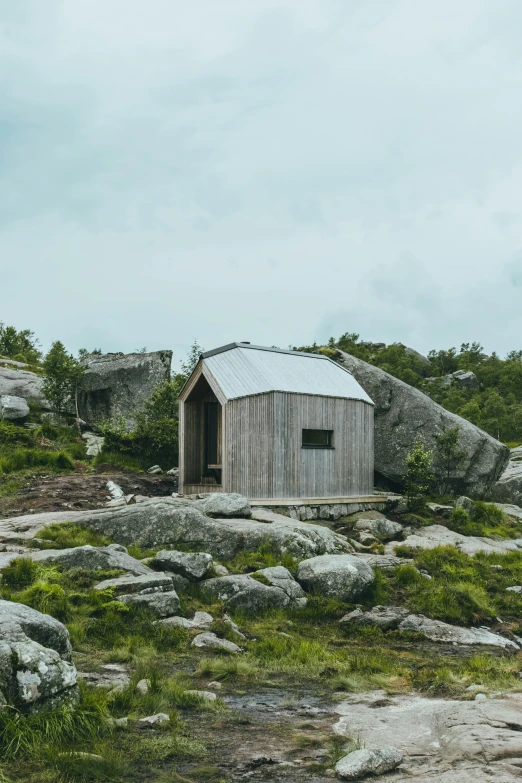 a small cabin sitting on top of a rocky hill, by Roar Kjernstad, unsplash, modernism, wooden toilets, galvalume metal roofing, with vegetation, half - length photo