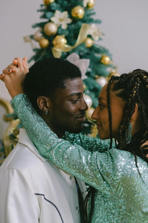 a man and woman dancing in front of a christmas tree, trending on pexels, lesbian embrace, with afro, green tones and golden charms, ( ( theatrical ) )