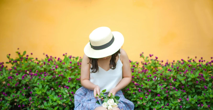 a woman sitting on a bench holding a bouquet of flowers, inspired by Clarice Beckett, pexels contest winner, white straw flat brimmed hat, pale yellow walls, vietnamese woman, gardening