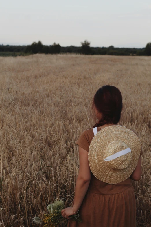 a woman standing in a wheat field holding a bunch of flowers, by Attila Meszlenyi, pexels contest winner, conceptual art, white straw flat brimmed hat, view from the back, panoramic shot, taken on iphone 14 pro