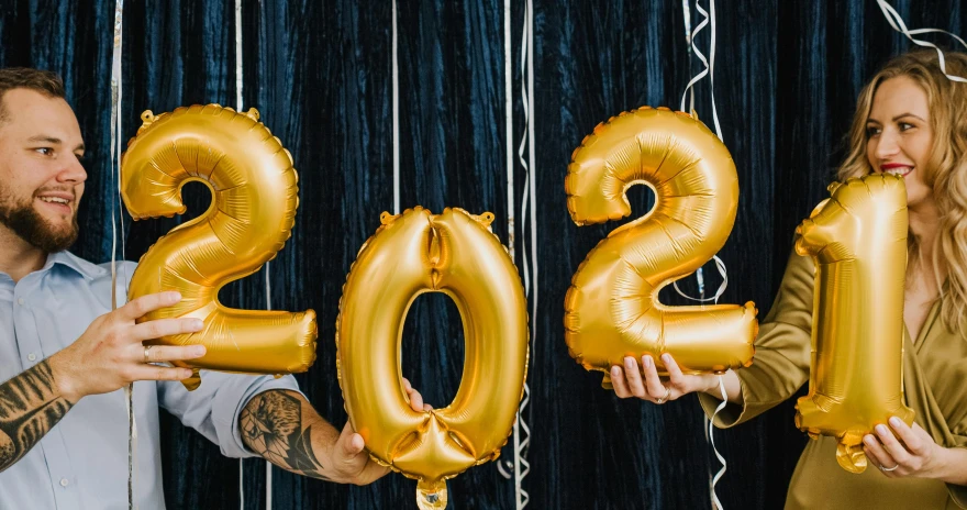 a man and a woman holding balloons in the shape of the numbers 2020, by Julia Pishtar, trending on unsplash, happening, gold linens, college party, thumbnail, reverse