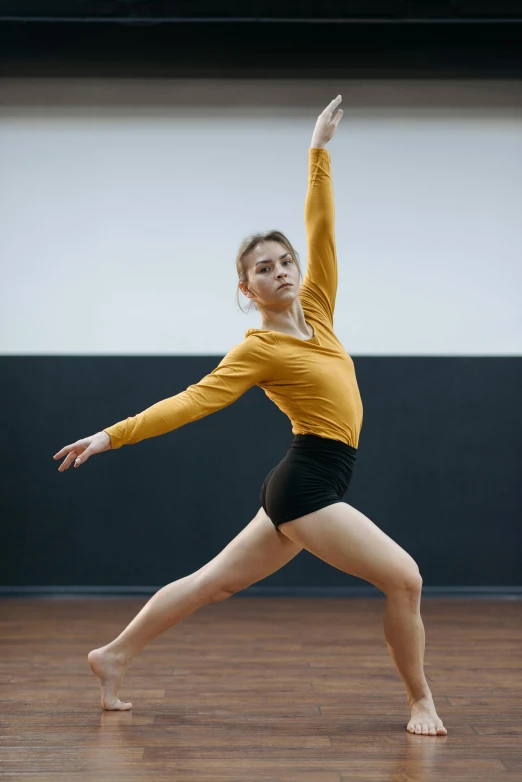 a woman in a yellow shirt is doing a dance, unsplash, arabesque, sydney sweeney, looking towards camera, shows a leg, university