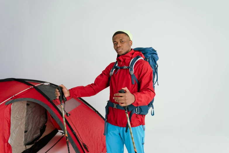 a man in a red jacket standing next to a red tent, trending on pexels, hurufiyya, wearing a blue jacket, ( ( dark skin ) ), climber, pack