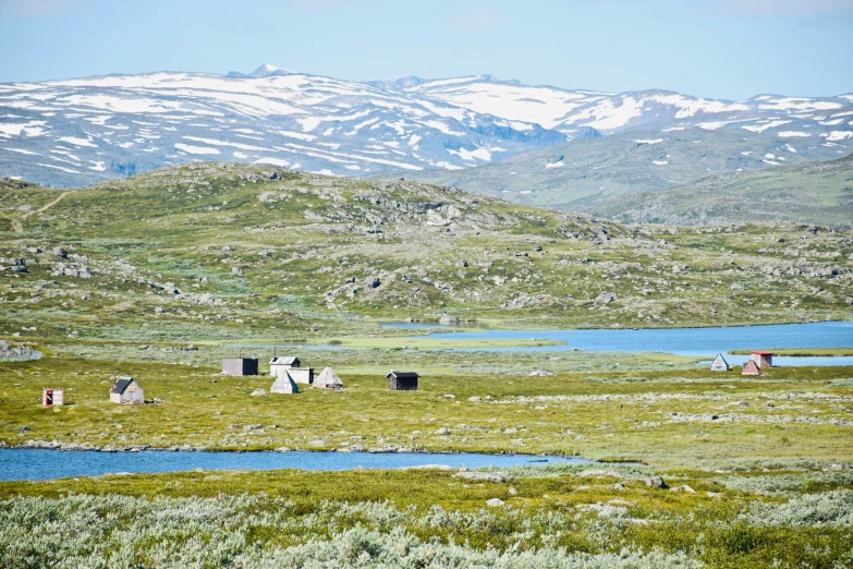 a body of water sitting on top of a lush green field, by Sigrid Hjertén, hurufiyya, huts, in the snow mountains, tourist photo