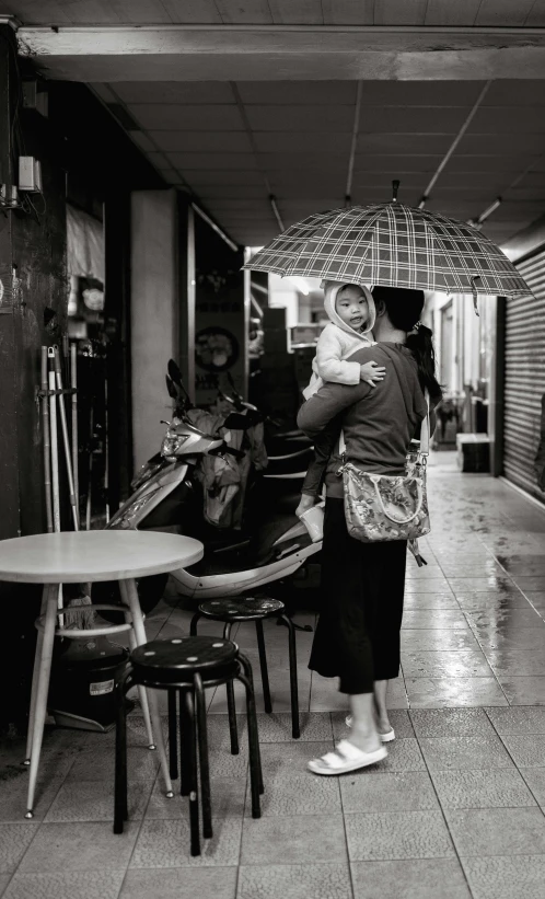 a woman holding a baby under an umbrella, by Joze Ciuha, bangkok, in a sidewalk cafe, yuli ban, jonathan ivy