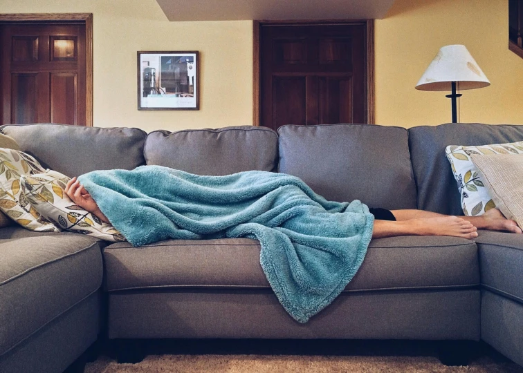 a man laying on top of a couch covered in a blanket, by Carey Morris, pexels contest winner, happening, with teal clothes, plague and fever. full body, snoring, couch desk