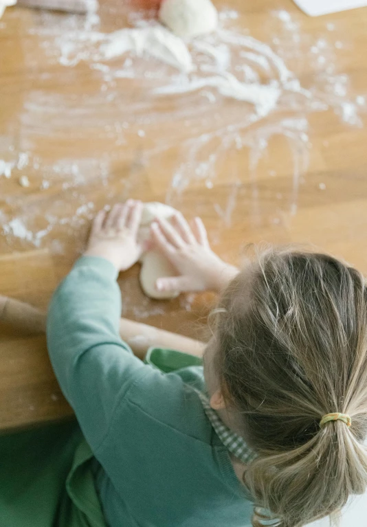 a little girl that is sitting at a table, covered in white flour, chopping hands, facing away, matt finish