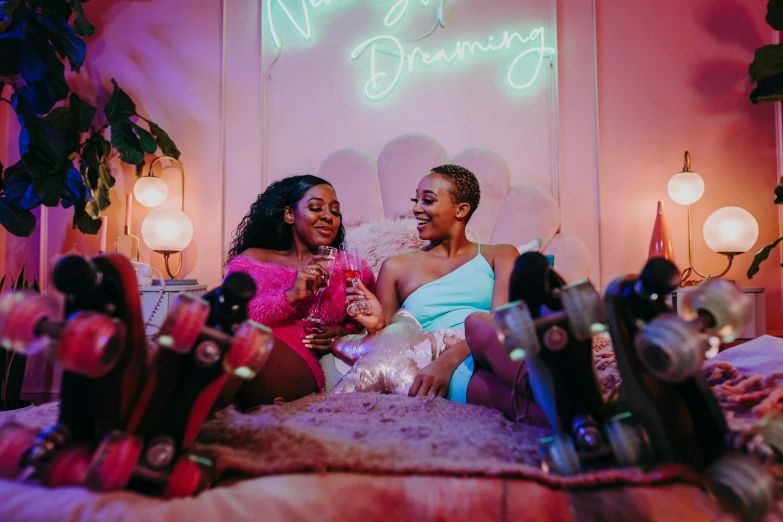 two women sitting on a bed in front of a neon sign, trending on pexels, neon hooves, essence, sitting in a lounge, celebrating