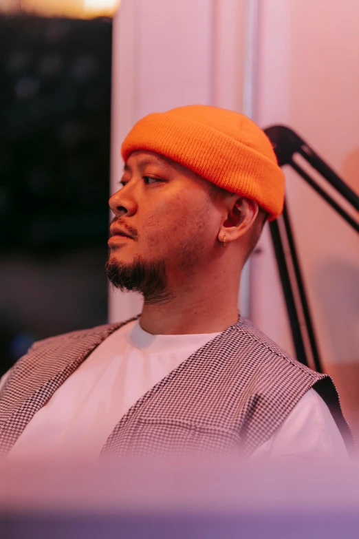 a man sitting in a chair wearing an orange hat, an album cover, inspired by Eddie Mendoza, unsplash, realism, asian male, headshot profile picture, standing in a dimly lit room, small chin