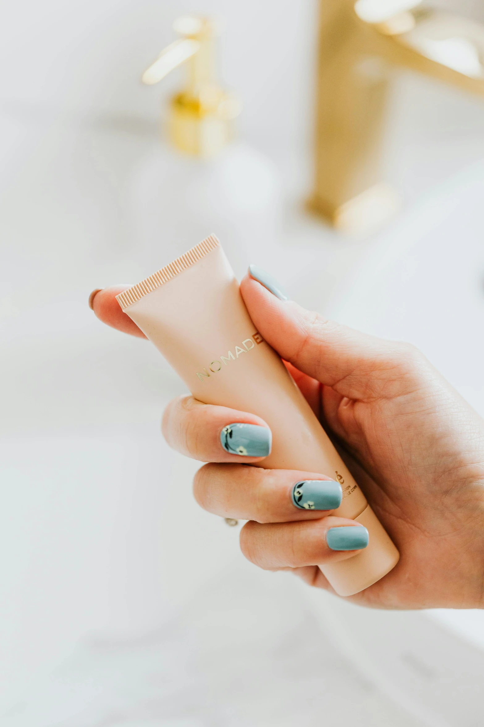 a woman holding a tube of cream in her hand, unsplash, art nouveau, turquoise gold details, on a white table, neat nails, jovana rikalo