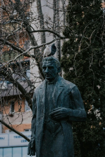 a statue of a man standing next to a tree, a statue, inspired by Ernő Grünbaum, unsplash contest winner, bird, whistler, grey, jan matejko and j.dickenson