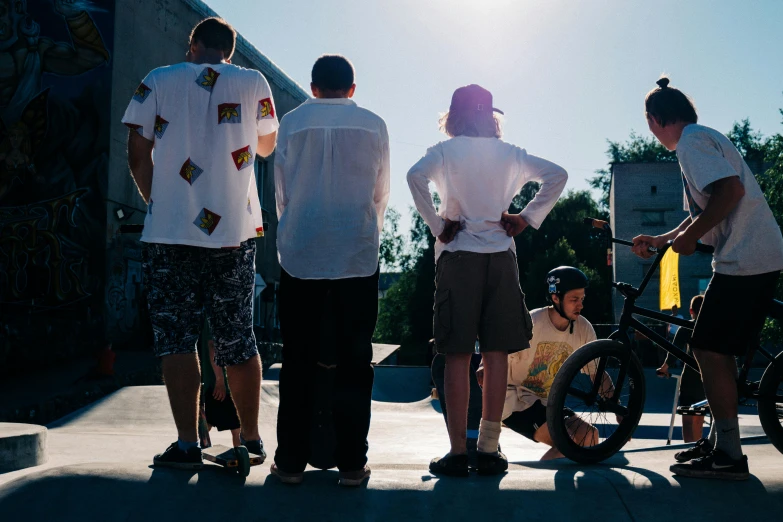 a group of people standing around a boy on a skateboard, unsplash, with his back turned, federation clothing, in the sun, mechanics