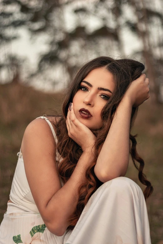 a woman in a white dress sitting on the ground, inspired by Elsa Bleda, trending on pexels, renaissance, dark lipstick, hand on cheek, young southern woman, curls