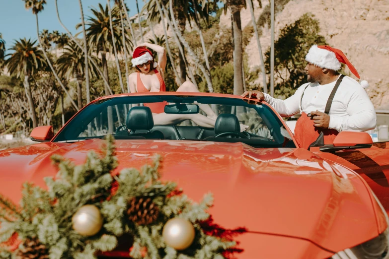 a man and woman sitting in a red sports car, by Julia Pishtar, pexels contest winner, wearing festive clothing, with palm trees in the back, santa, rex orange county