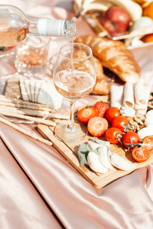 a table topped with plates of food and glasses of wine, picnic, pink, bubbly, on a wooden plate