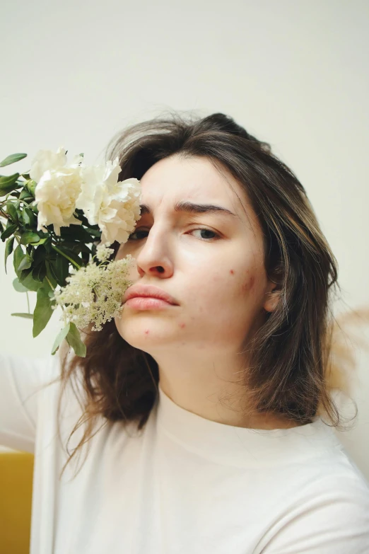 a woman holding a bunch of flowers in front of her face, an album cover, inspired by Elsa Bleda, trending on pexels, aestheticism, portrait androgynous girl, annoyed facial expression, joe keery, white freckles