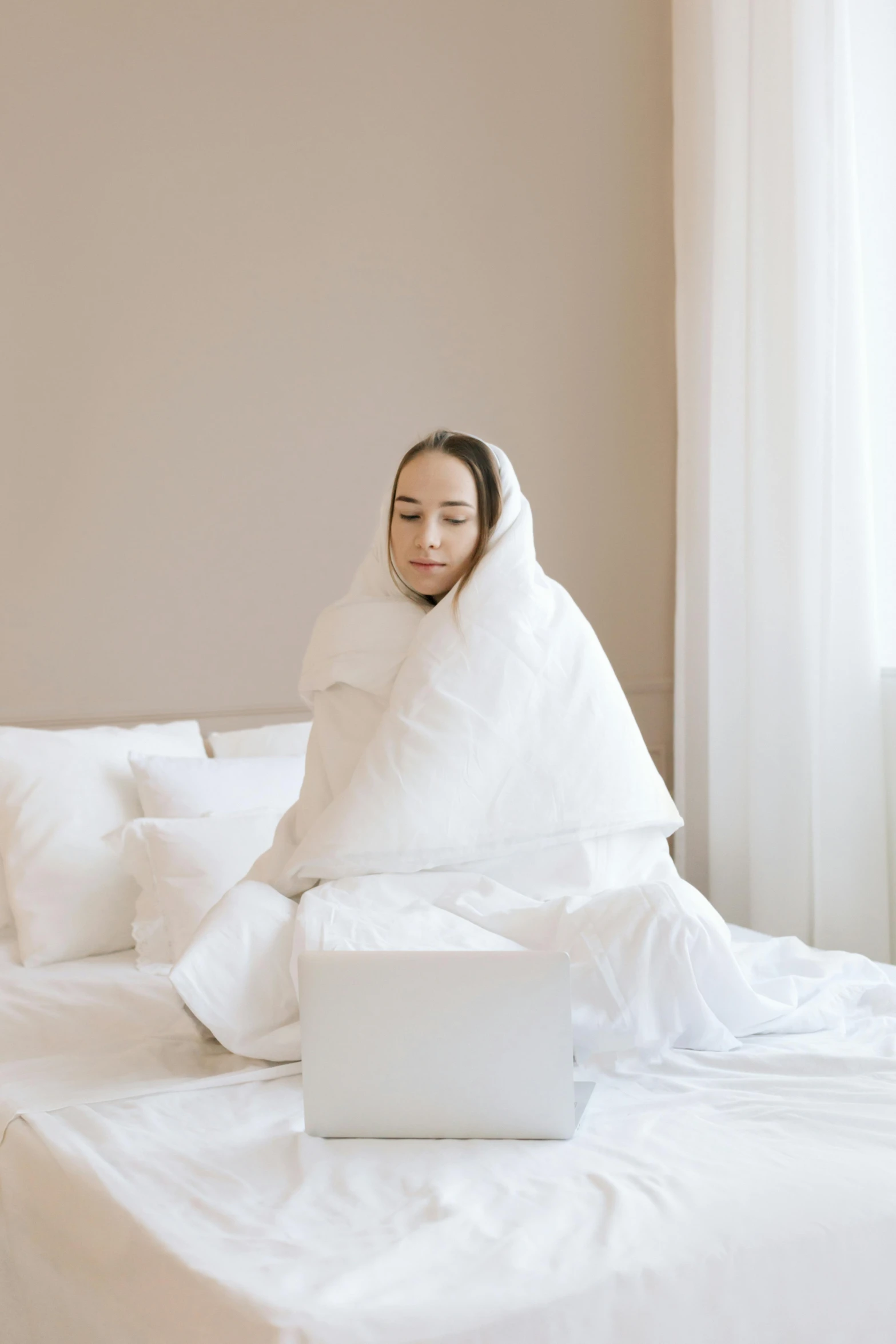 a woman sitting on a bed with a laptop under a blanket, white puffy outfit, cooling, premium, stressing out