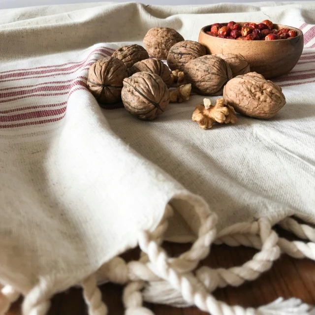 a wooden bowl filled with nuts on top of a table, a still life, inspired by Géza Dósa, featured on pinterest, large draped cloth, red left eye stripe, close-up product photo, handcrafted