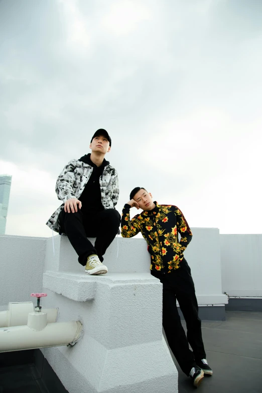 a couple of men sitting on top of a building, an album cover, inspired by Wang Duo, unsplash, patterned clothing, set on singaporean aesthetic, standing on a rooftop, official store photo