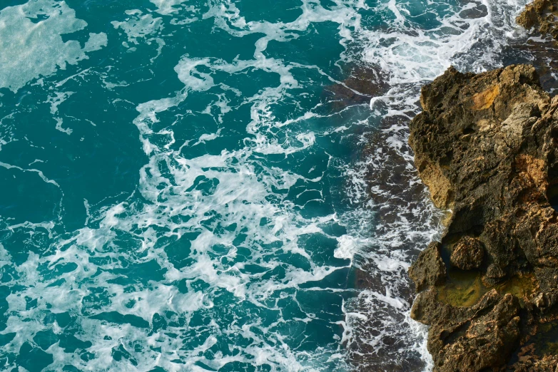 a large body of water next to a rocky shore, pexels contest winner, cresting waves and seafoam, cerulean, looking down a cliff, full frame image