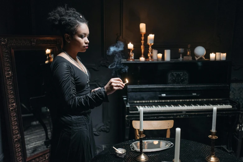 a woman in a black dress standing in front of a piano, inspired by Carrie Mae Weems, pexels contest winner, vanitas, lit candles, smoking woman, a seance, abigail larson