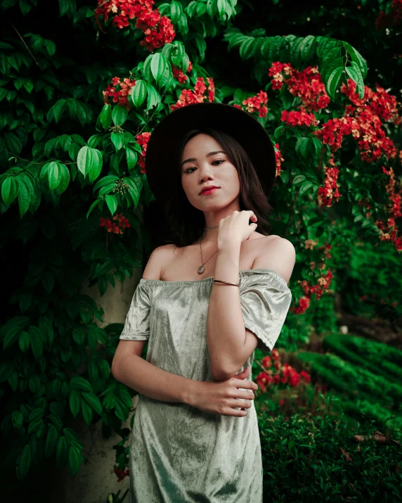 a woman standing in front of a bush with red flowers, a colorized photo, unsplash, wearing a chocker and cute hat, set on singaporean aesthetic, green dress, wearing an elegant outfit