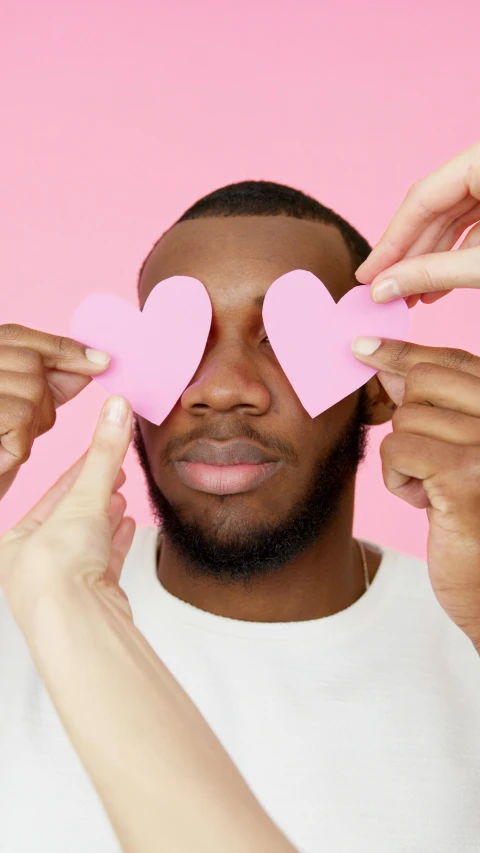 a man holding two pink hearts in front of his face, by Dulah Marie Evans, trending on pexels, diverse eyes!, paper cutouts of plain colors, groomed eyebrows, lgbtq